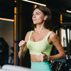 Kobieta w sportowym stroju biegnie na bieżni w siłowni.