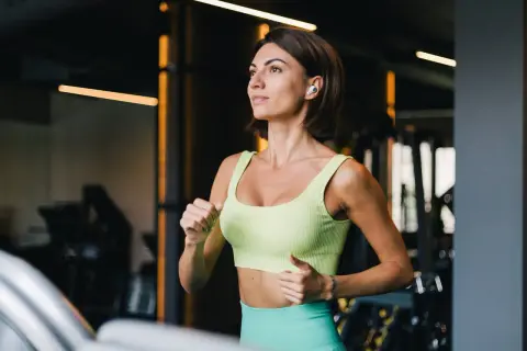 Kobieta w sportowym stroju biegnie na bieżni w siłowni.