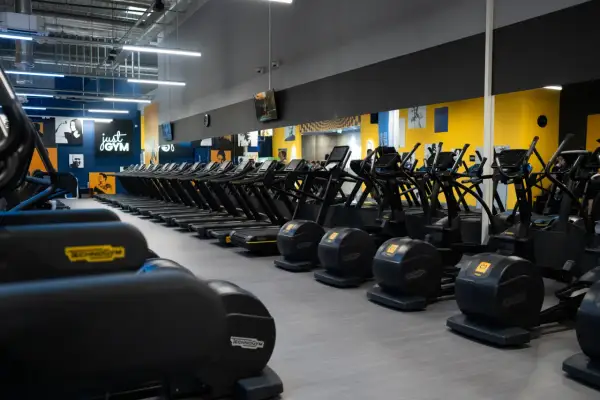 Rzędy bieżni i orbitreków w siłowni Just Gym. Chcesz wiedzieć, jak wejść na Multisport? Tu zaczynasz trening!