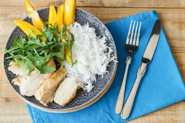Idealne danie, co jeść po treningu: grillowany kurczak, ryż, mango i rukola na talerzu.
